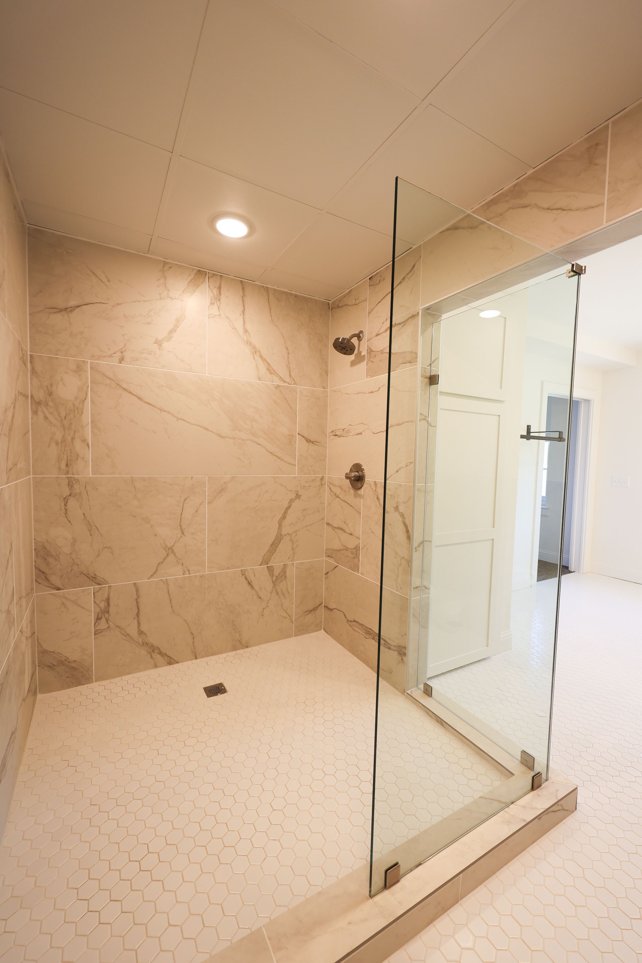 A modern bathroom with a glass shower enclosure, marble tiles, and a hexagonal tile floor.