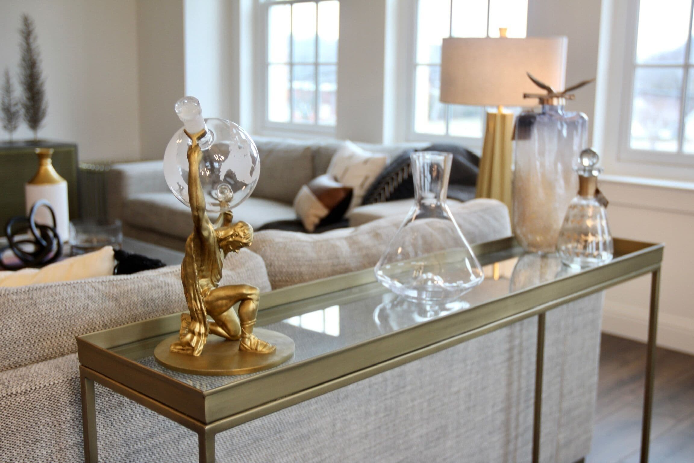 Ein modernes Wohnzimmer mit einem Glastisch, einer goldenen Statue und dekorativem Glaswaren.