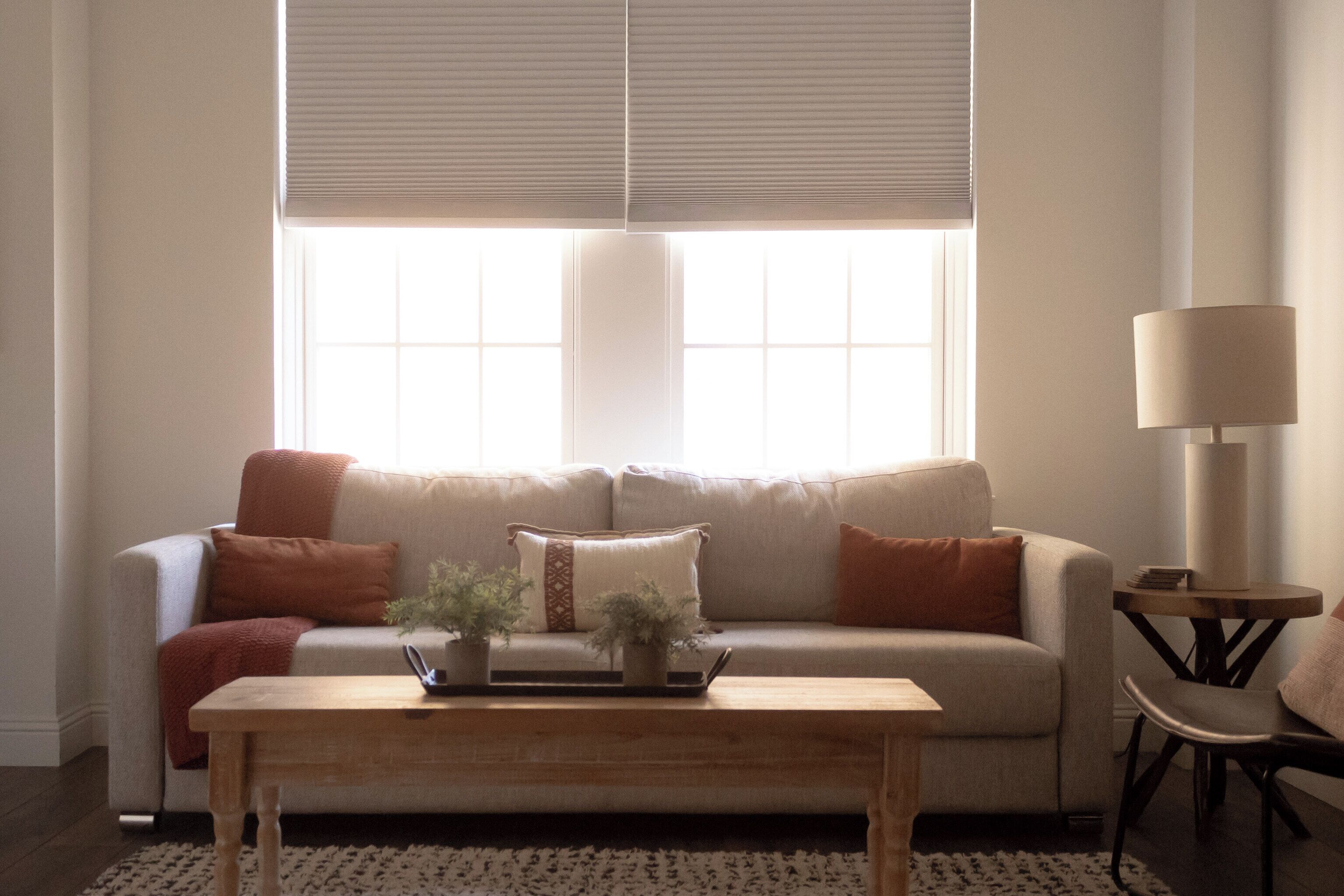 A living room with a sofa, a coffee table, a lamp, and a window with blinds.