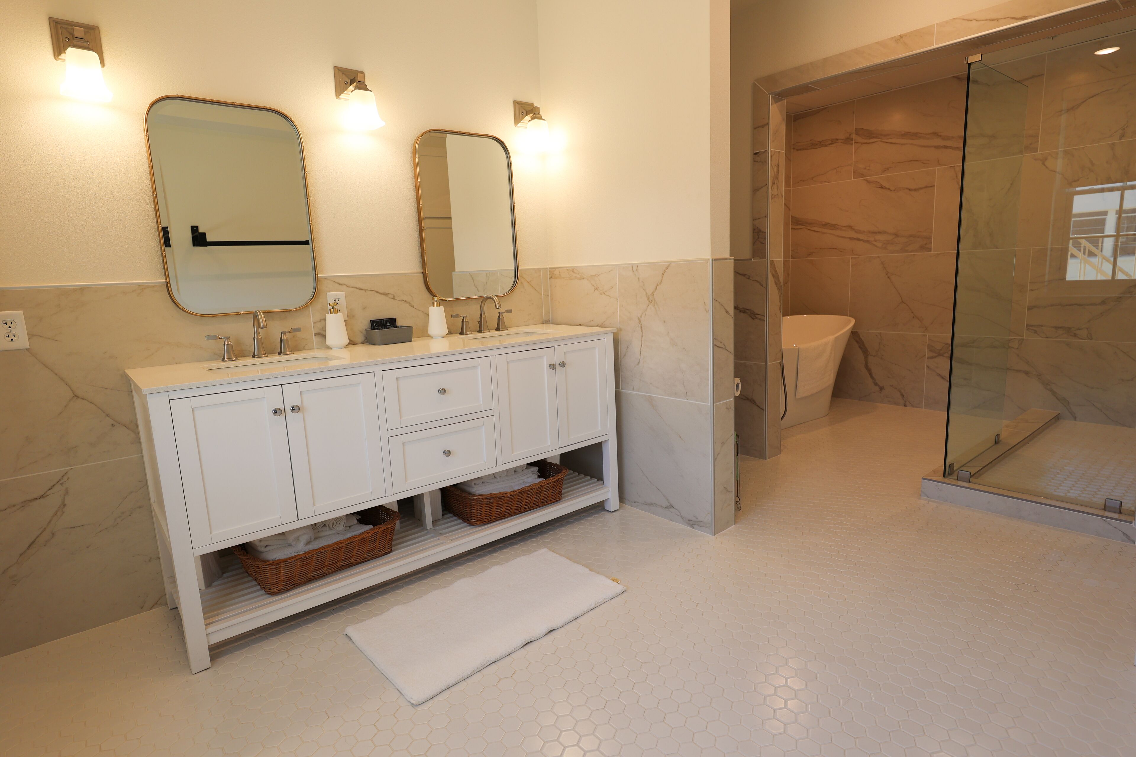 A bathroom with a white vanity, two mirrors, a glass shower enclosure, and hexagonal tile flooring.