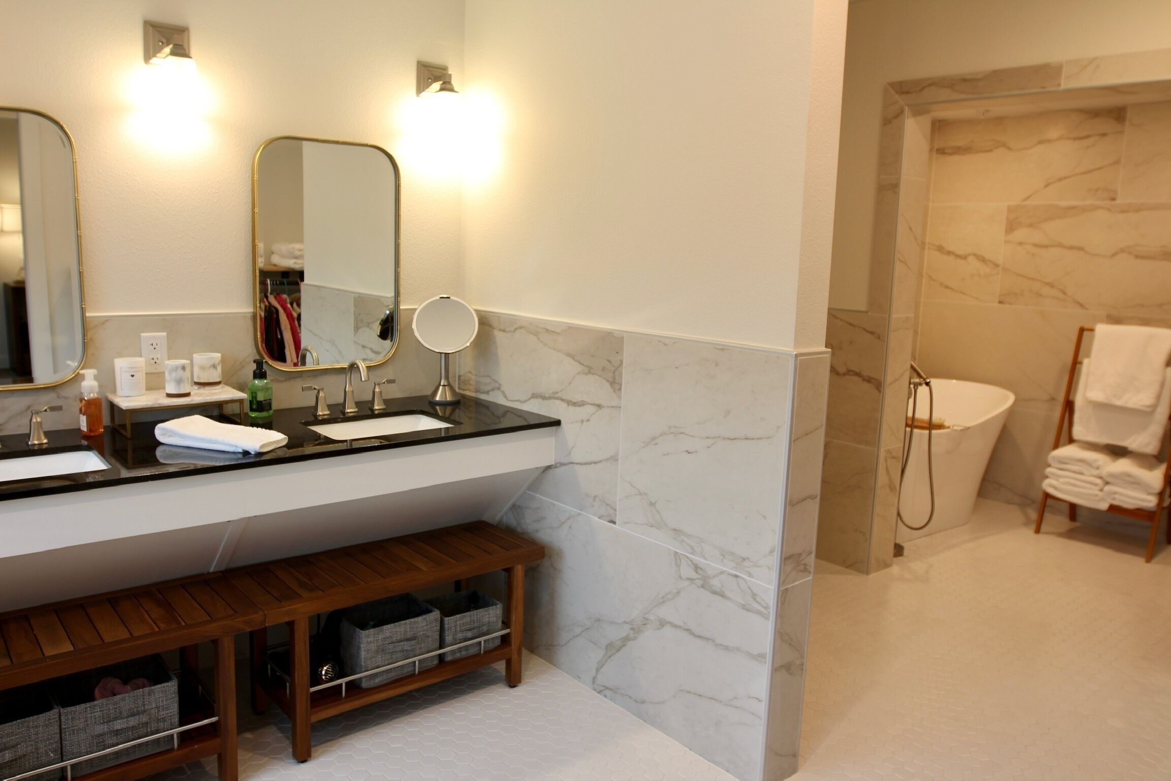 A modern bathroom with a marble wall, a bathtub, a sink with a mirror, and a vanity with storage.