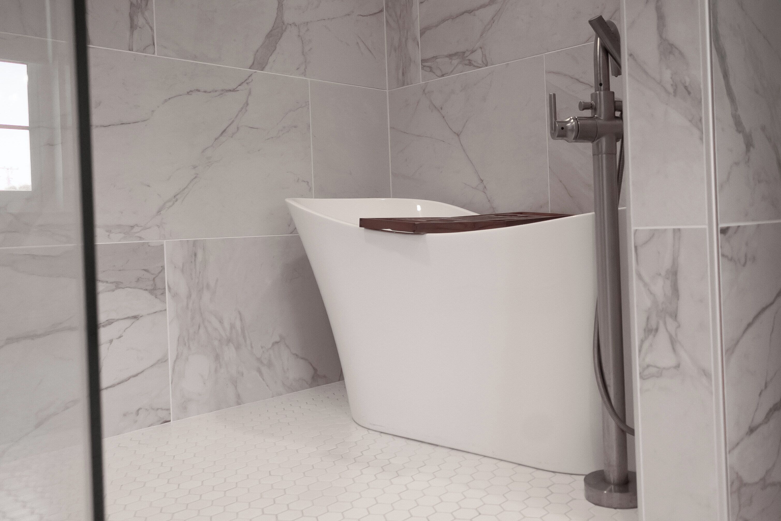 A modern bathroom with a white bathtub, a glass shower enclosure, and marble walls.