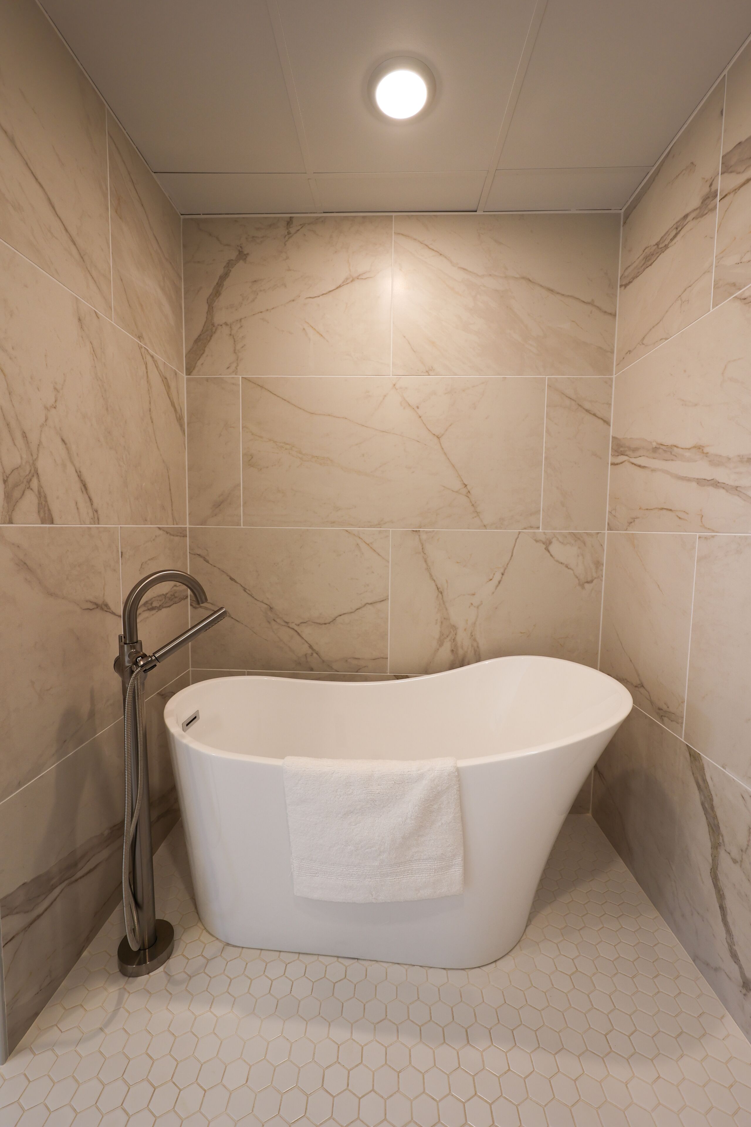 A modern bathroom with a freestanding bathtub, a handheld showerhead, and hexagonal floor tiles.