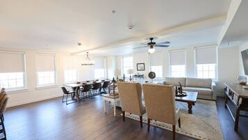 A spacious living room with a dining area, a ceiling fan, and large windows.