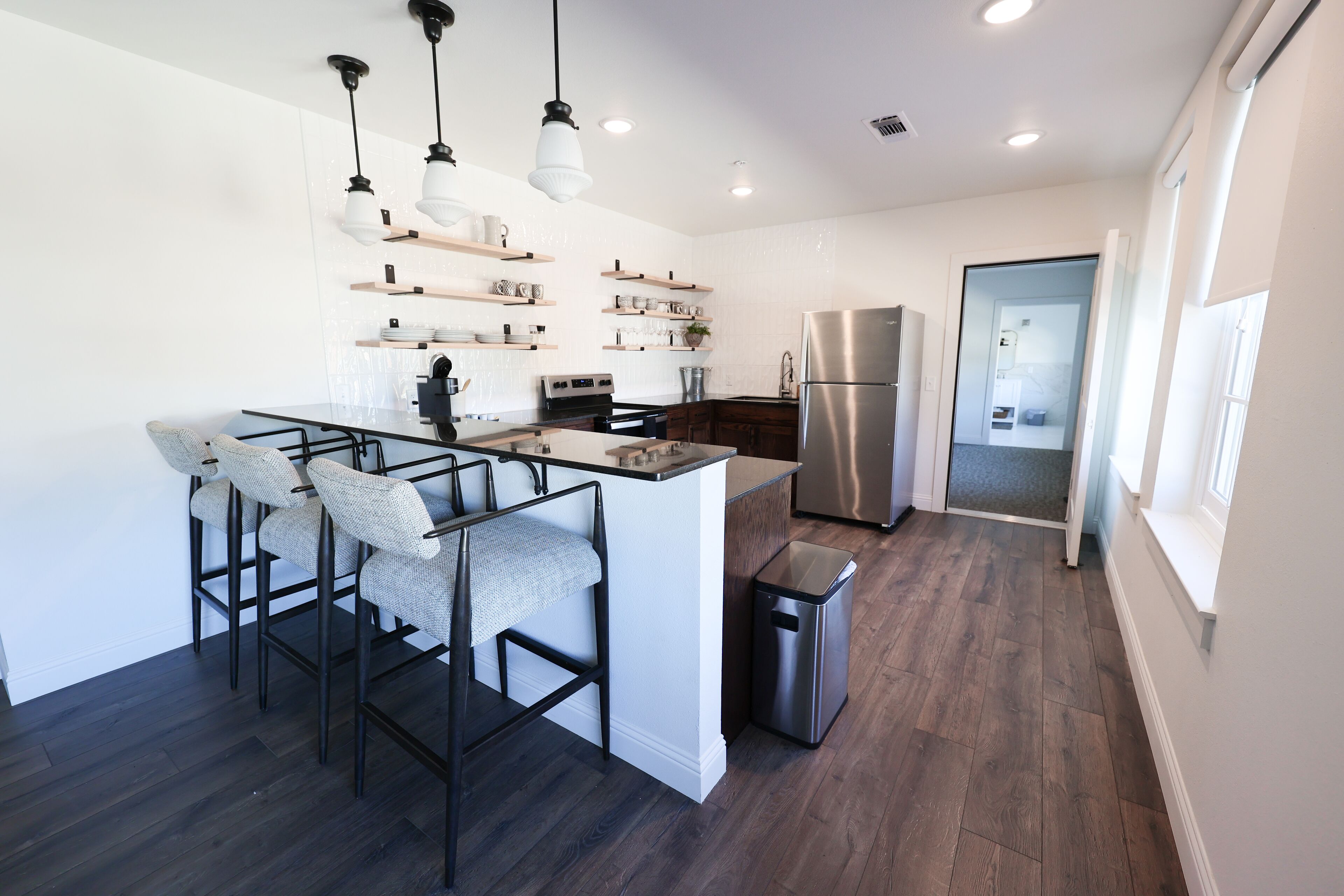 Una cocina moderna con una isla central, taburetes de bar, iluminación colgante y estanterías empotradas.