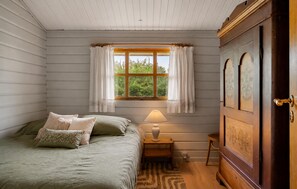 A bedroom with a bed, a nightstand with a lamp, a wooden wardrobe, and a window with curtains. - Gorgeous home in Hadsund with WiFi (Hadsund)
