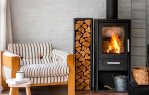 A cozy room with a striped sofa, a wood-burning stove, and a stack of firewood. - Gorgeous home in Hadsund with WiFi (Hadsund)