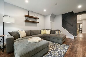Un salon moderne avec un canapé d’angle, une table d’appoint, un lampadaire et un tapis à motifs.