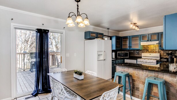 A kitchen with a wooden table and white chairs, blue cabinets, and a stone backsplash. - Spacious 2,500 Sq Ft Wichita Home -3 Showers-2 Tubs-Near Base & Arena (Wichita)