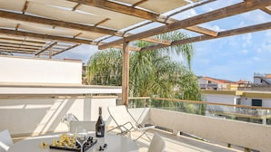 Une terrasse sur le toit avec un échiquier, un verre à vin et une bouteille, entourée d’une pergola en bois et de palmiers.