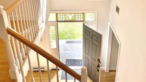 Un escalier avec des balustrades blanches et une main courante en bois menant à une porte dotée d’un panneau de verre.