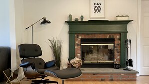 Un salon avec une cheminée, un fauteuil moderne, une lampe sur pied et un tableau encadré au mur.