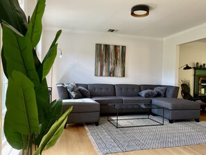 Ein modernes Wohnzimmer mit einem Ecksofa, einem Couchtisch und einer großen Pflanze.
