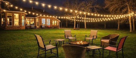 A backyard with a fire pit, outdoor furniture, and string lights.