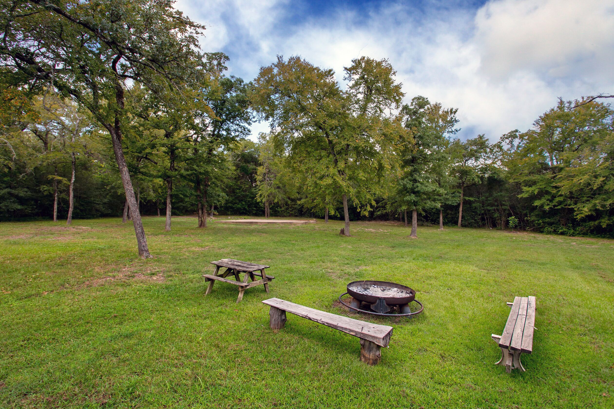 A grassy outdoor area with picnic tables and a fire pit.