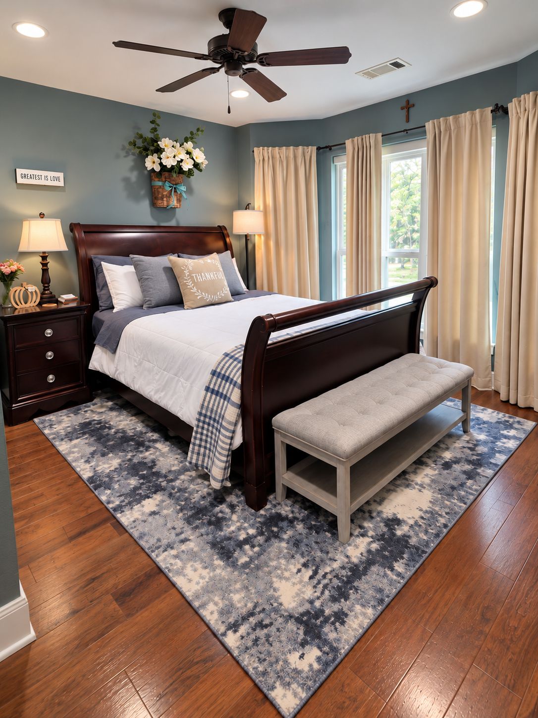 A bedroom with a bed, bedside tables, a bench, a ceiling fan, and a window with curtains.