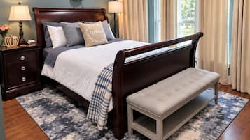 A bedroom with a bed, bedside tables, a bench, a ceiling fan, and a window with curtains.