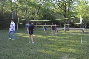 Un grupo de personas jugando voleibol en un parque con césped y árboles de fondo.