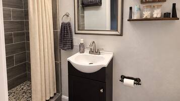 A bathroom with a shower, a sink, a toilet, a mirror, and a shelf with toiletries.