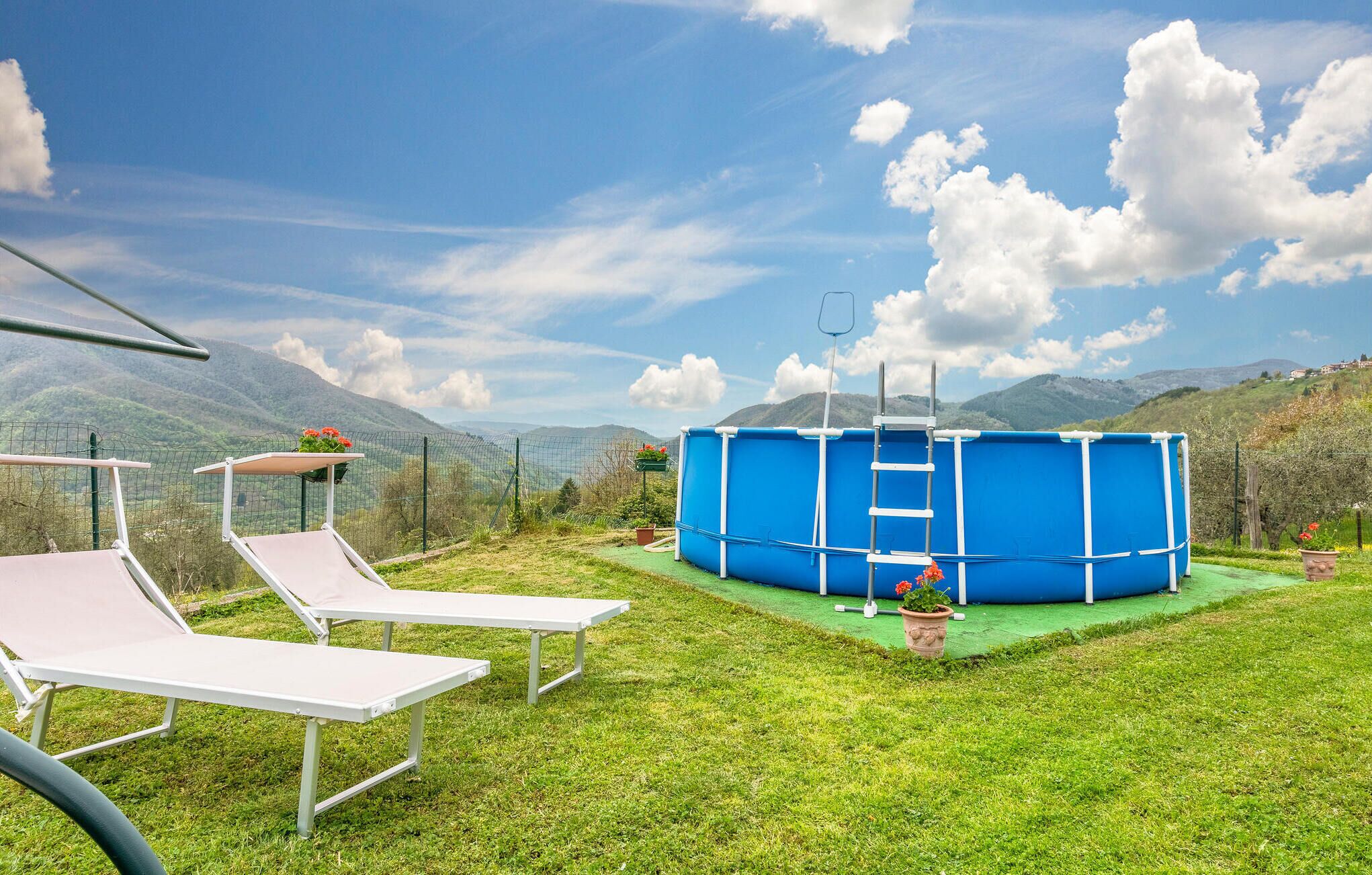 A pool area with a blue pool, two white lounge chairs, and a green deck.