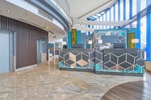 A hotel lobby with a reception desk, a curved ceiling, and a view of the sky through large windows. - eXo Square Heidelberg-Schwetzingen - By SuperFly Hotels (Schwetzingen)