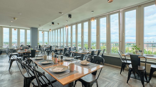 Un comedor amplio con varias mesas y sillas, y grandes ventanales que ofrecen vistas de la ciudad.