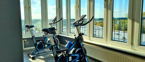 Two stationary bikes in a room with large windows offering a city view.