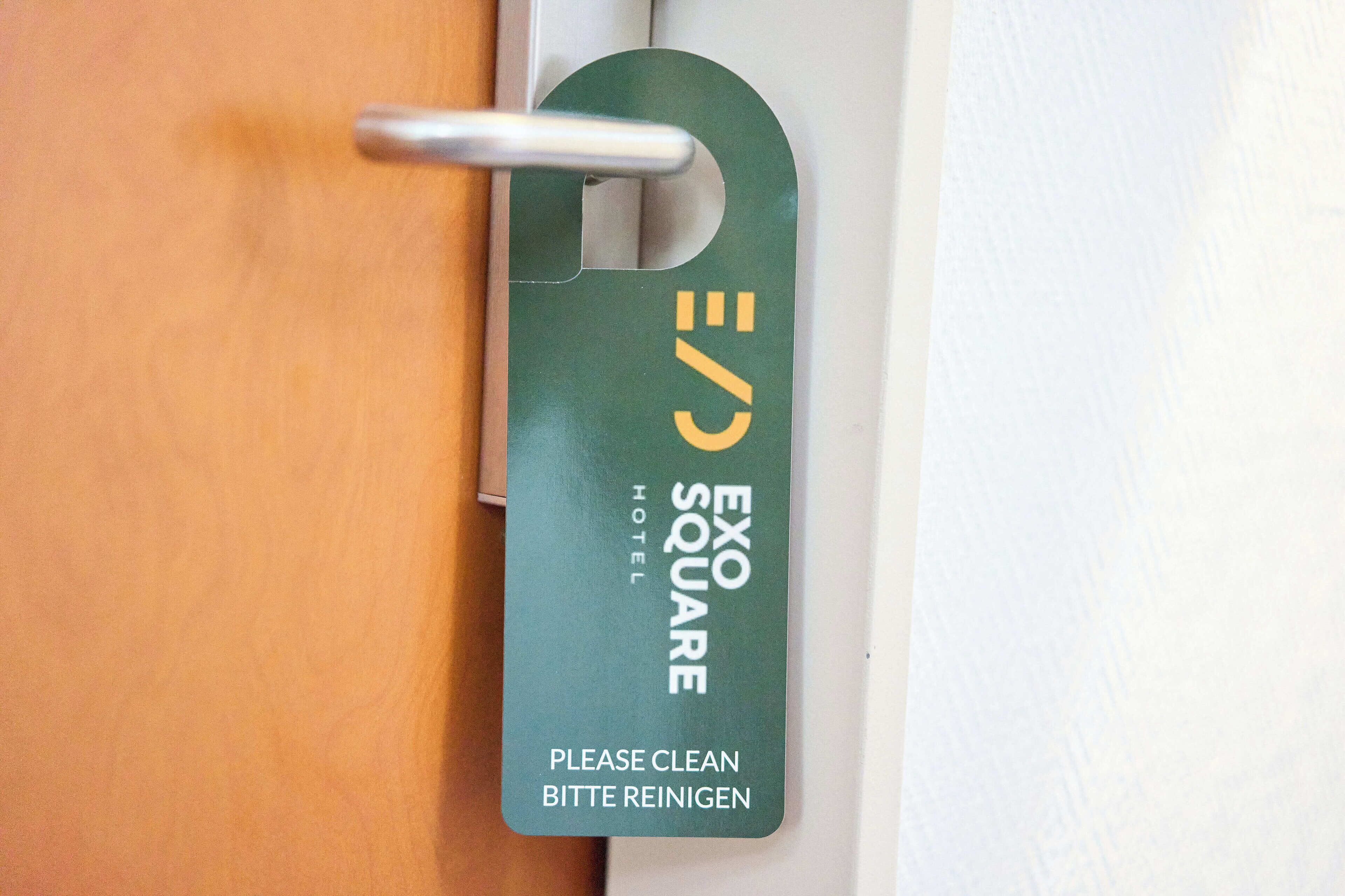 A hotel room door with a keycard holder displaying the Exo Square Hotel logo and a "Please clean" instruction.