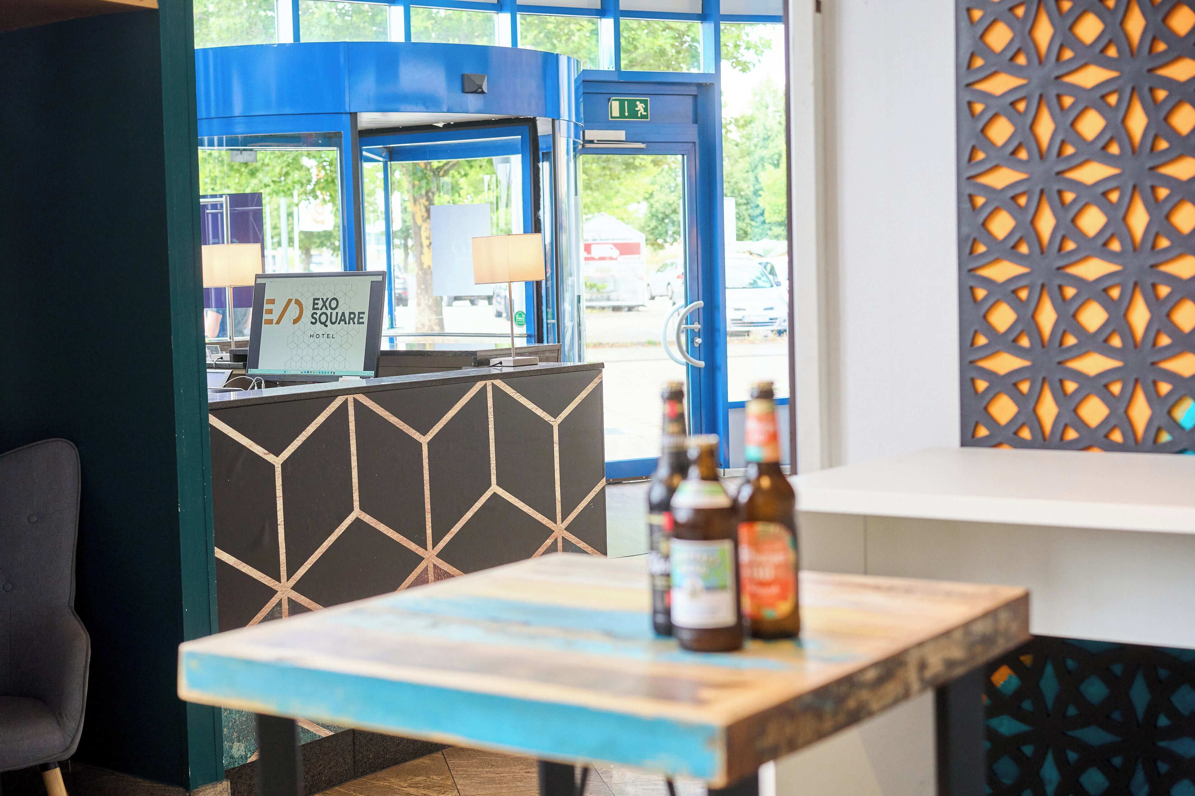 A hotel reception desk with a computer, a lamp, and a table with bottles.