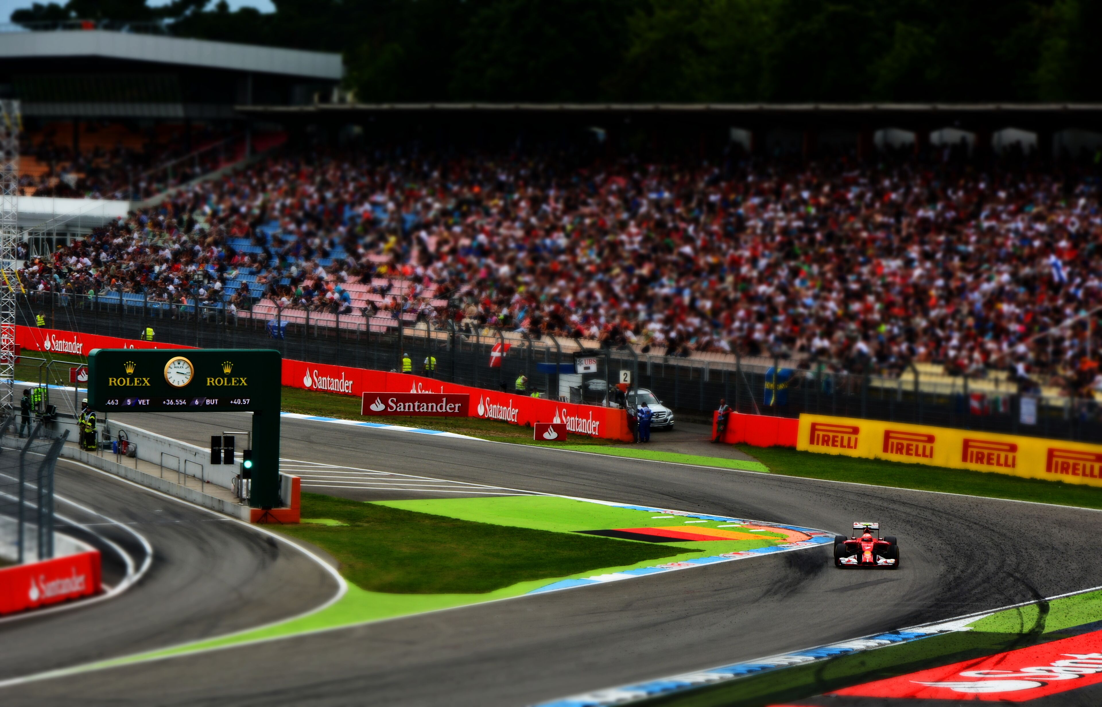A race track with a car in motion, surrounded by spectators.