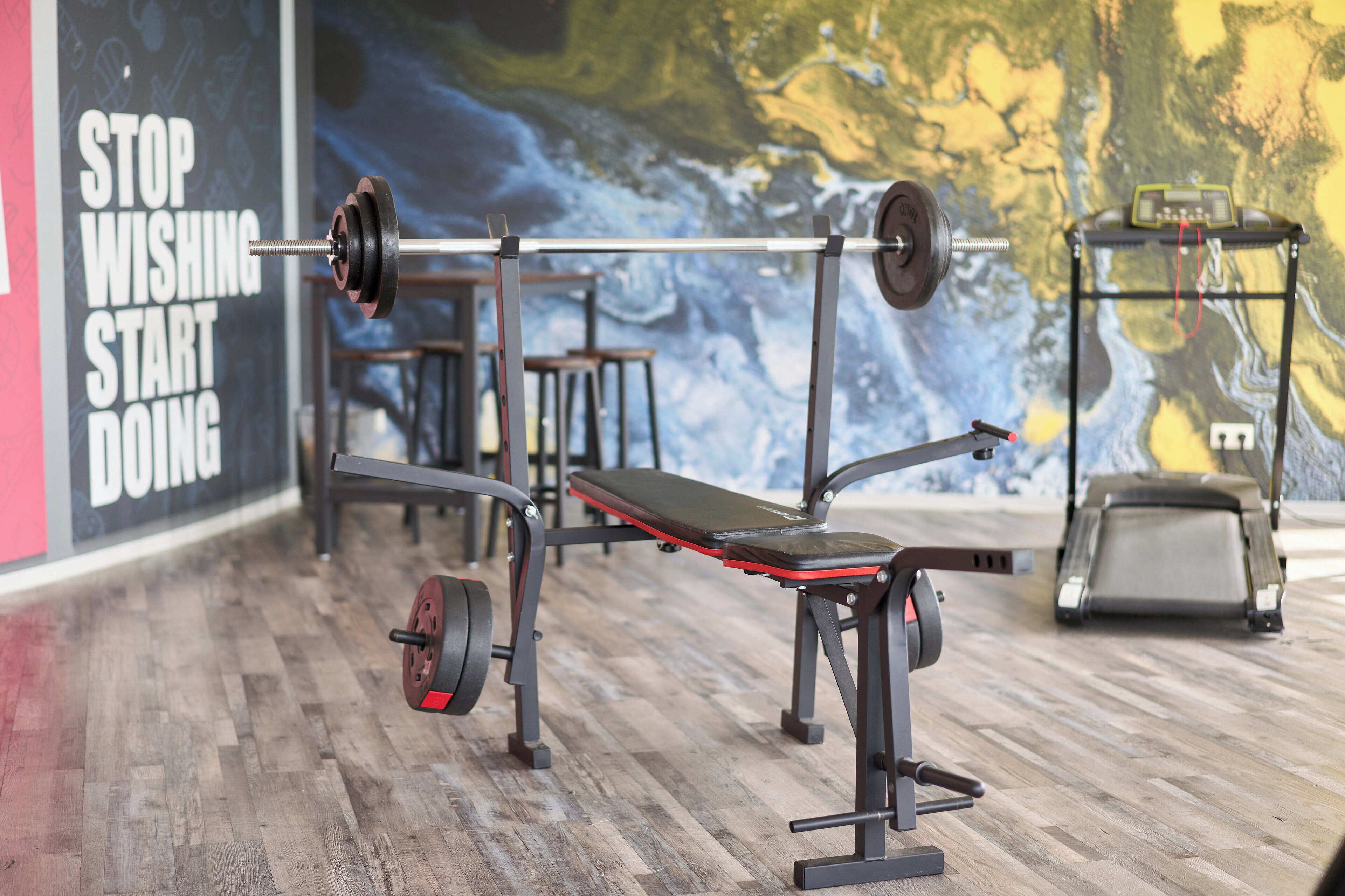 A gym with a bench press, a treadmill, and a wall with motivational text.