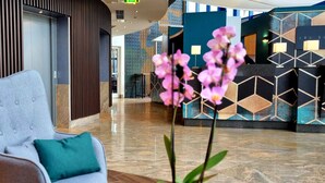 Un vestíbulo moderno con mostrador de recepción, un área de estar con una silla y cojín, y una planta de orquídea decorativa.