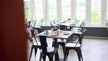 Un comedor con mesas y sillas, ventanas amplias con vistas, y piso de madera.