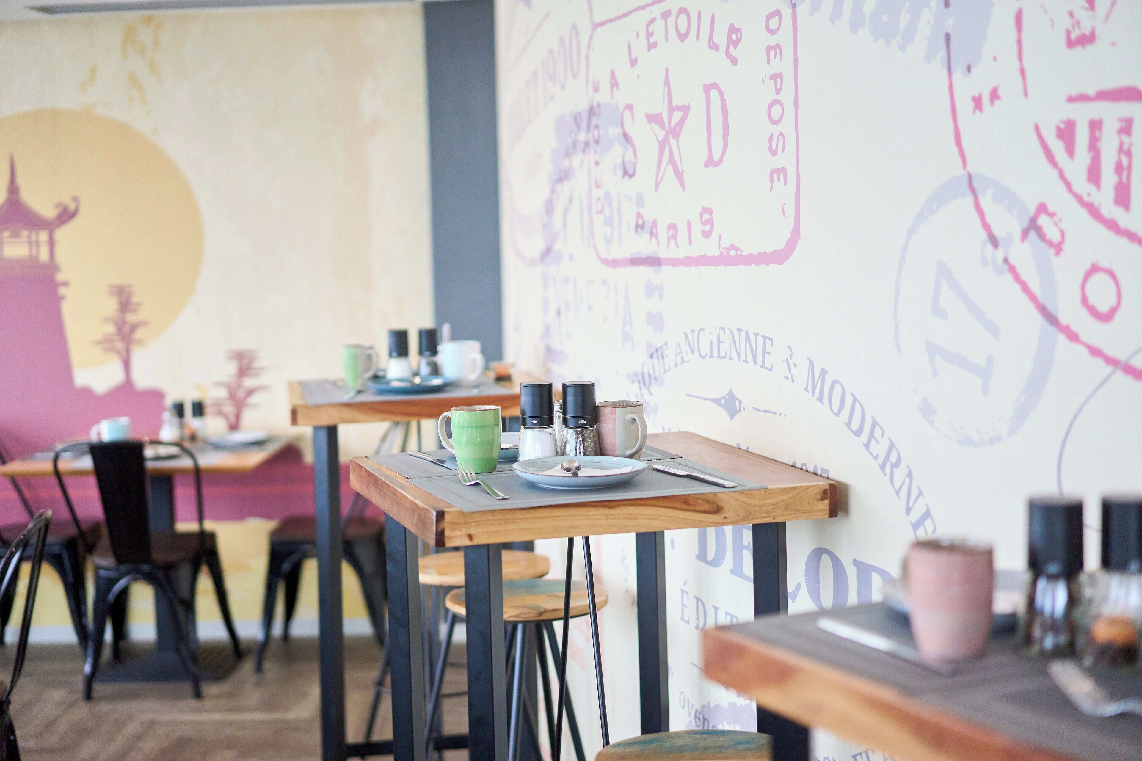 L'intérieur d'un café, avec des tables, des chaises et un mur orné de motifs artistiques.