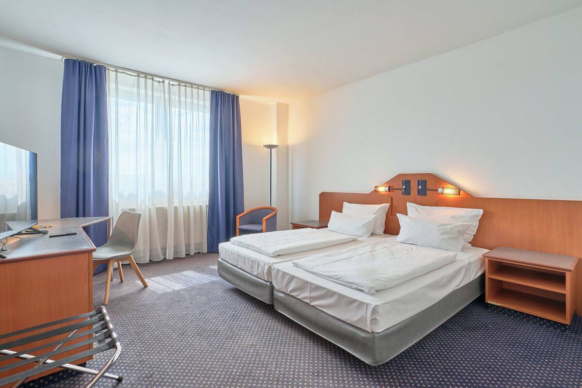 Habitación de hotel con dos camas, un escritorio, una silla, una lámpara y un televisor.