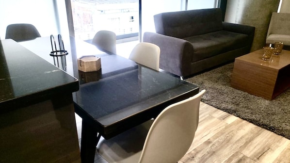 A modern living room with a black table, white chairs, a dark sofa, and a small wooden coffee table. - Central location, close to mall, restaurants, bars, markets & safe location. (Pereira)