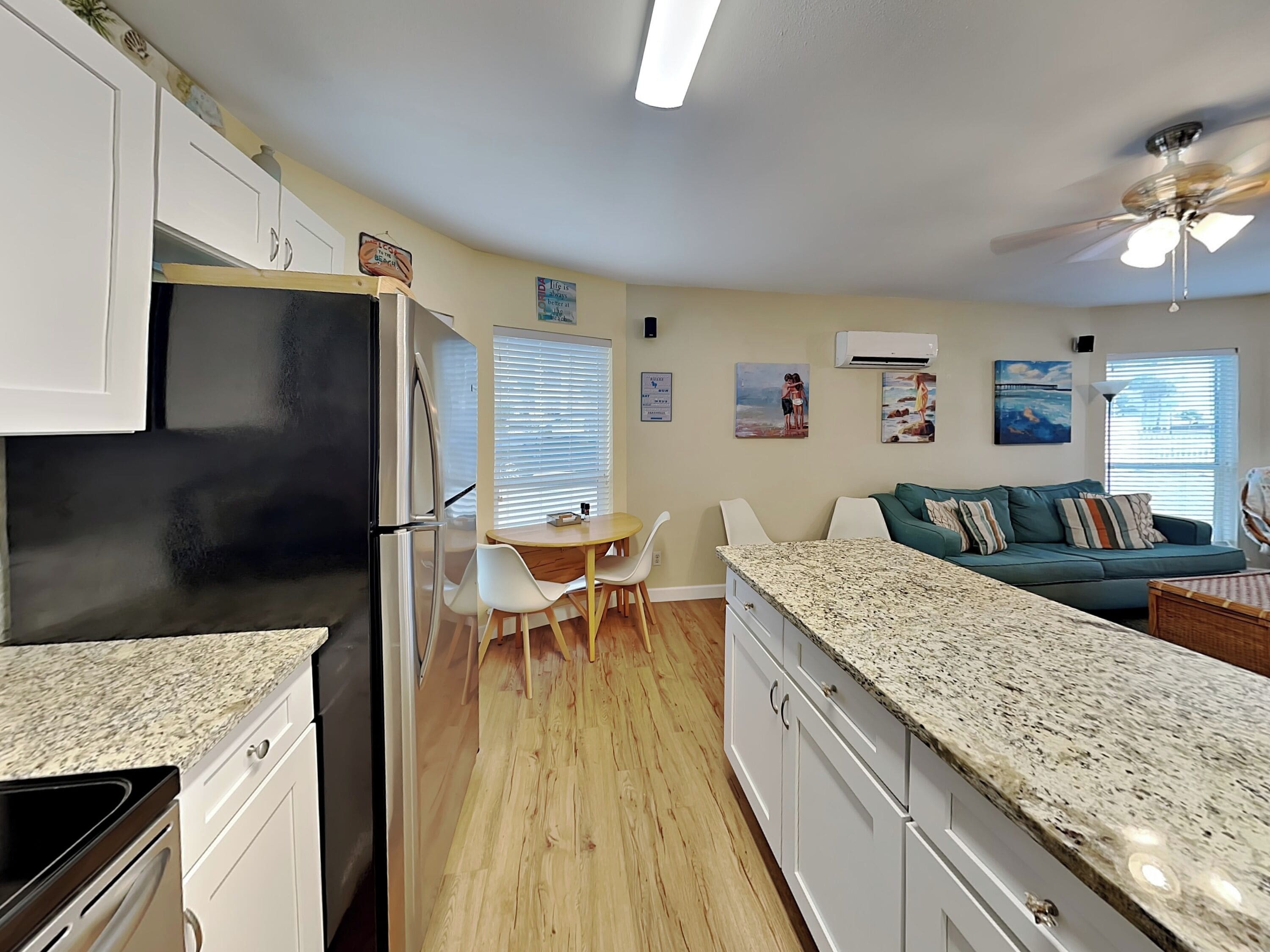 A modern kitchen with white cabinets, a black refrigerator, a granite countertop, and a dining area with white chairs.