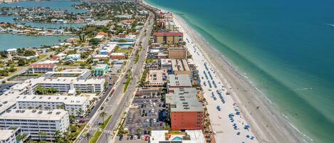 Vista aérea de una ciudad costera con una extensa playa, un puerto deportivo y una mezcla de edificios comerciales y residenciales.