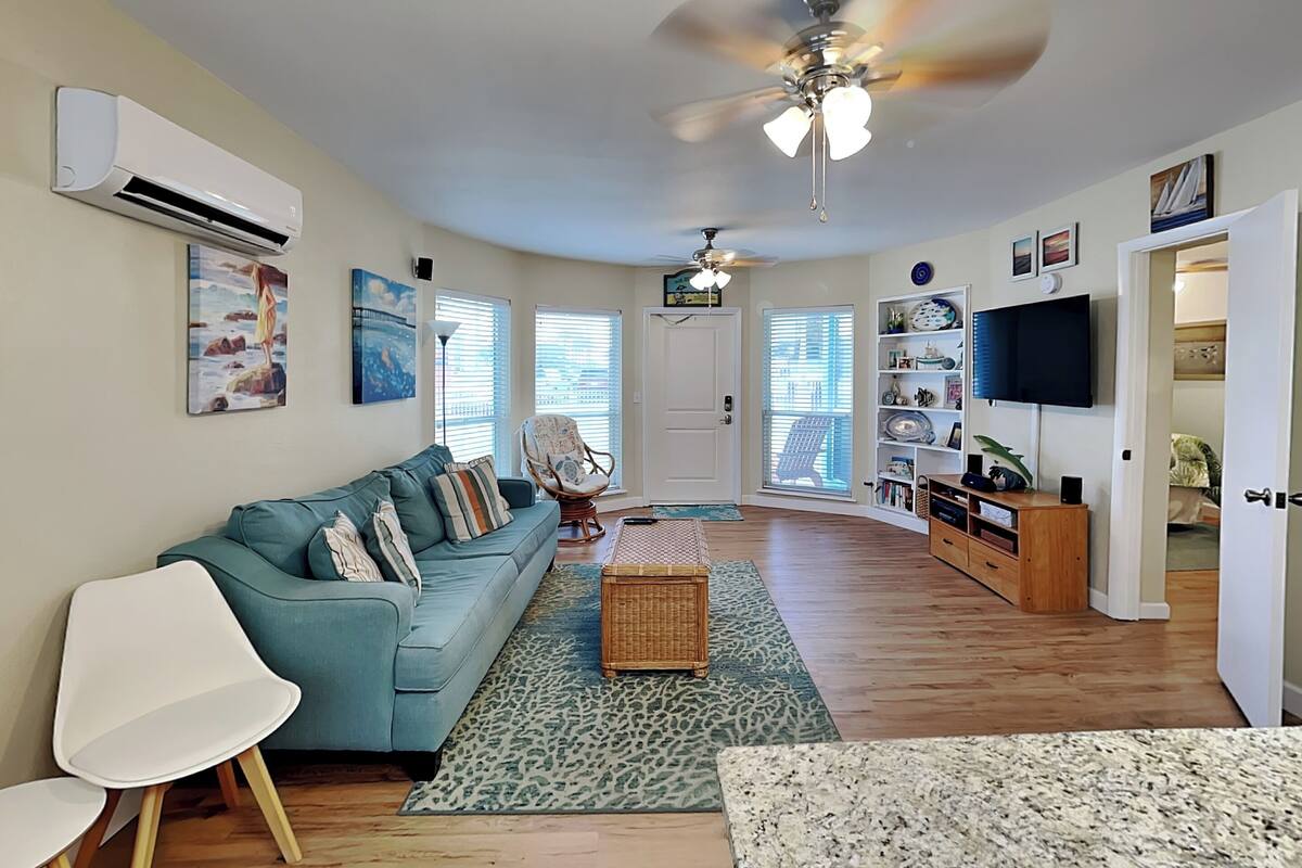 A modern living room with a blue sofa, white chairs, a ceiling fan, and a TV on a wooden stand.