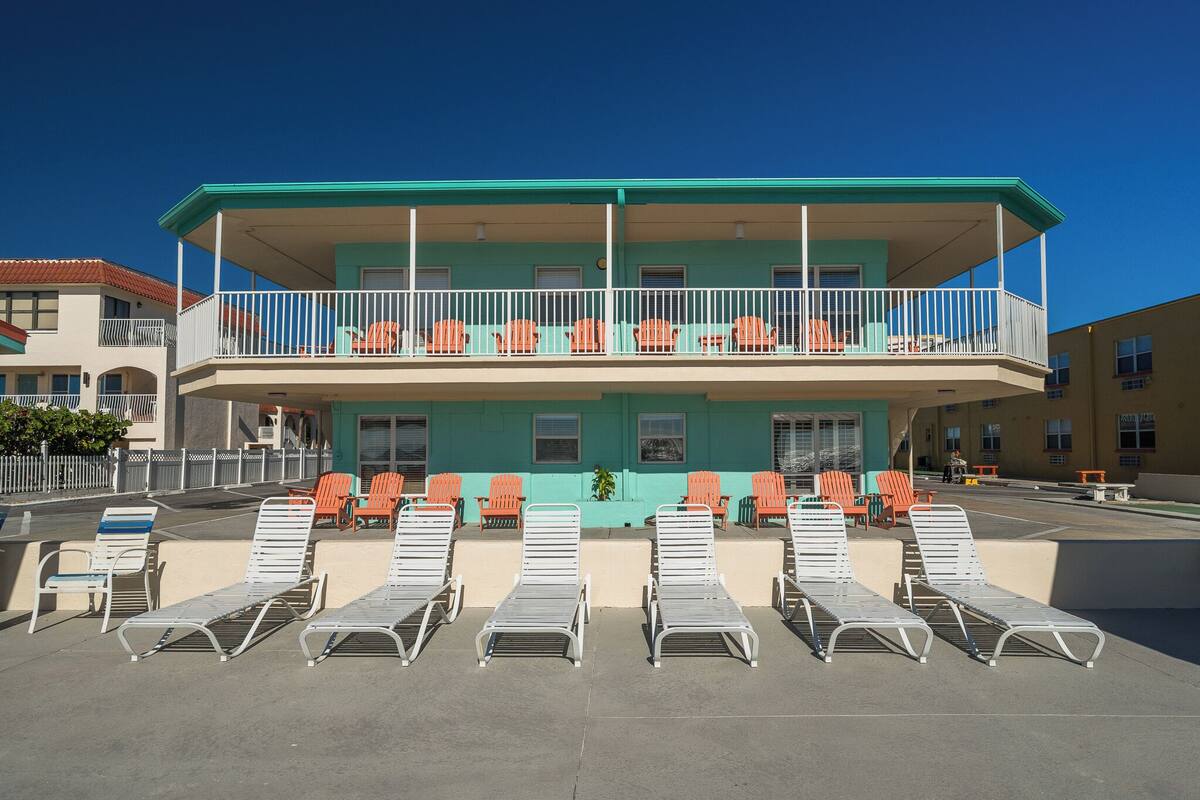 A two-story building with a balcony, outdoor seating area with lounge chairs, and a clear blue sky.