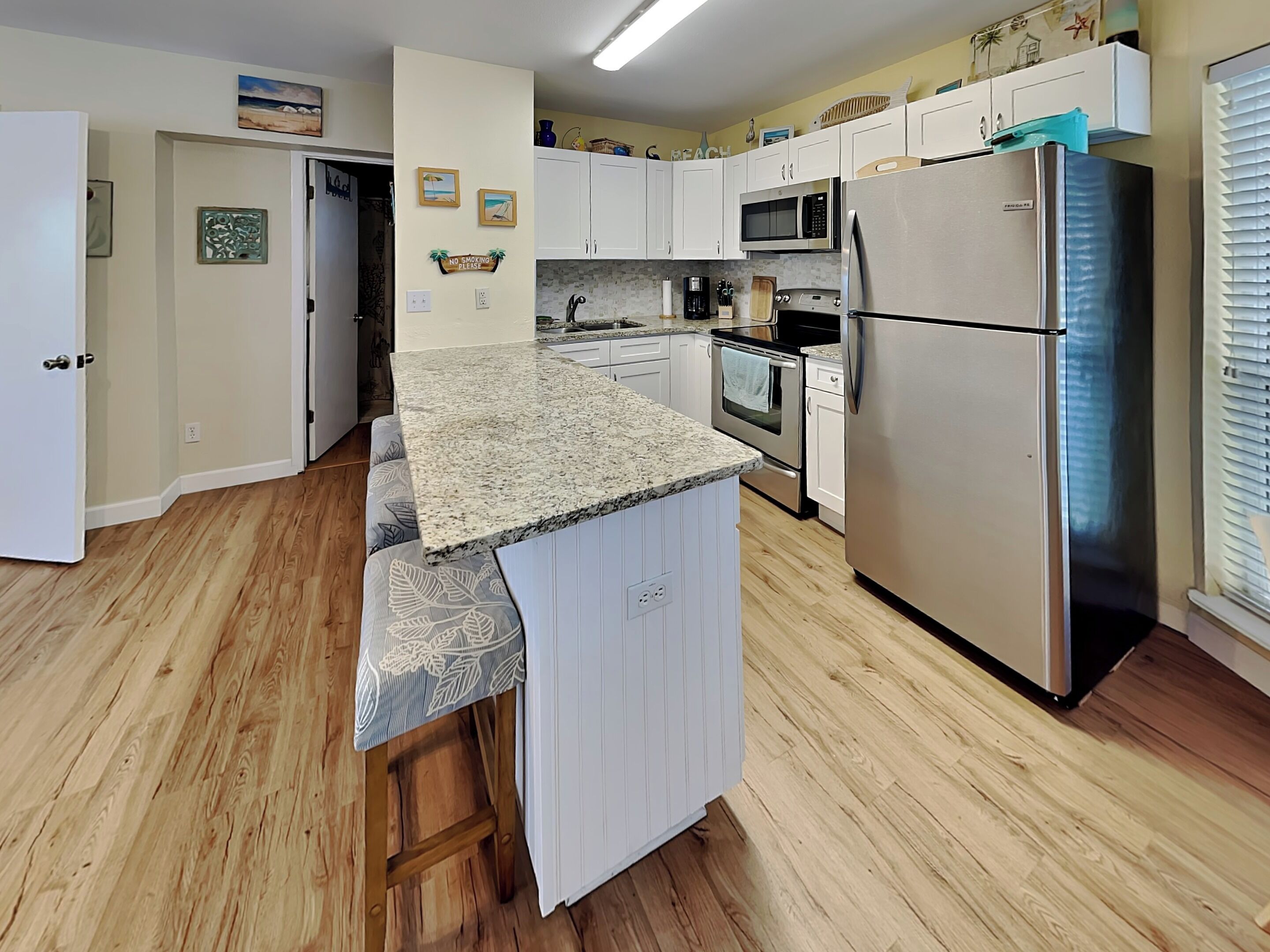 A kitchen with wooden flooring, white cabinets, a granite countertop, stainless steel appliances, and a small island with a bench.