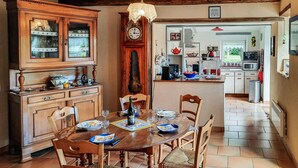 A dining area with a wooden table set for four, surrounded by wooden chairs. A large wooden cabinet with glass doors is to the left, and a kitchen area is visible in the background. - 2 bedroom gorgeous home in Concarneau (concarneau)
