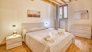 Un dormitorio con cama, mesita de noche, cómoda, radiador y ventana con cortinas.