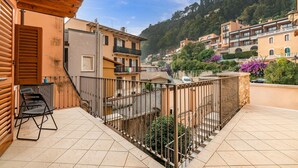Un balcón con vistas a un pueblo en la ladera, con edificios de tejas de arcilla, una pérgola de madera y una barandilla de metal.