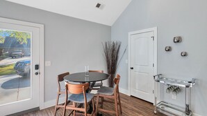 A dining area with a round table, four wooden chairs, a vase with branches, and a white door.