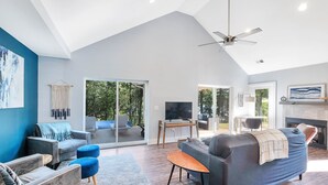A spacious living room with a large gray sofa, blue armchairs, and a wooden coffee table. There is a television and a fireplace.