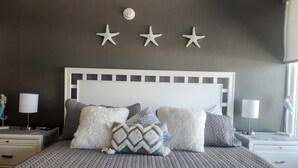 Ein Schlafzimmer mit einem großen Bett, zahlreichen Kissen, einem Kopfteil und dekorativen Seesternen an der Wand.
