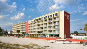 Ein mehrstöckiges Hotel mit roter und beiger Fassade direkt am Strand, bewölkter Himmel.