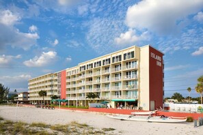 Un hôtel à plusieurs étages, doté d’une façade rouge et beige, situé sur une plage sous un ciel dégagé.
