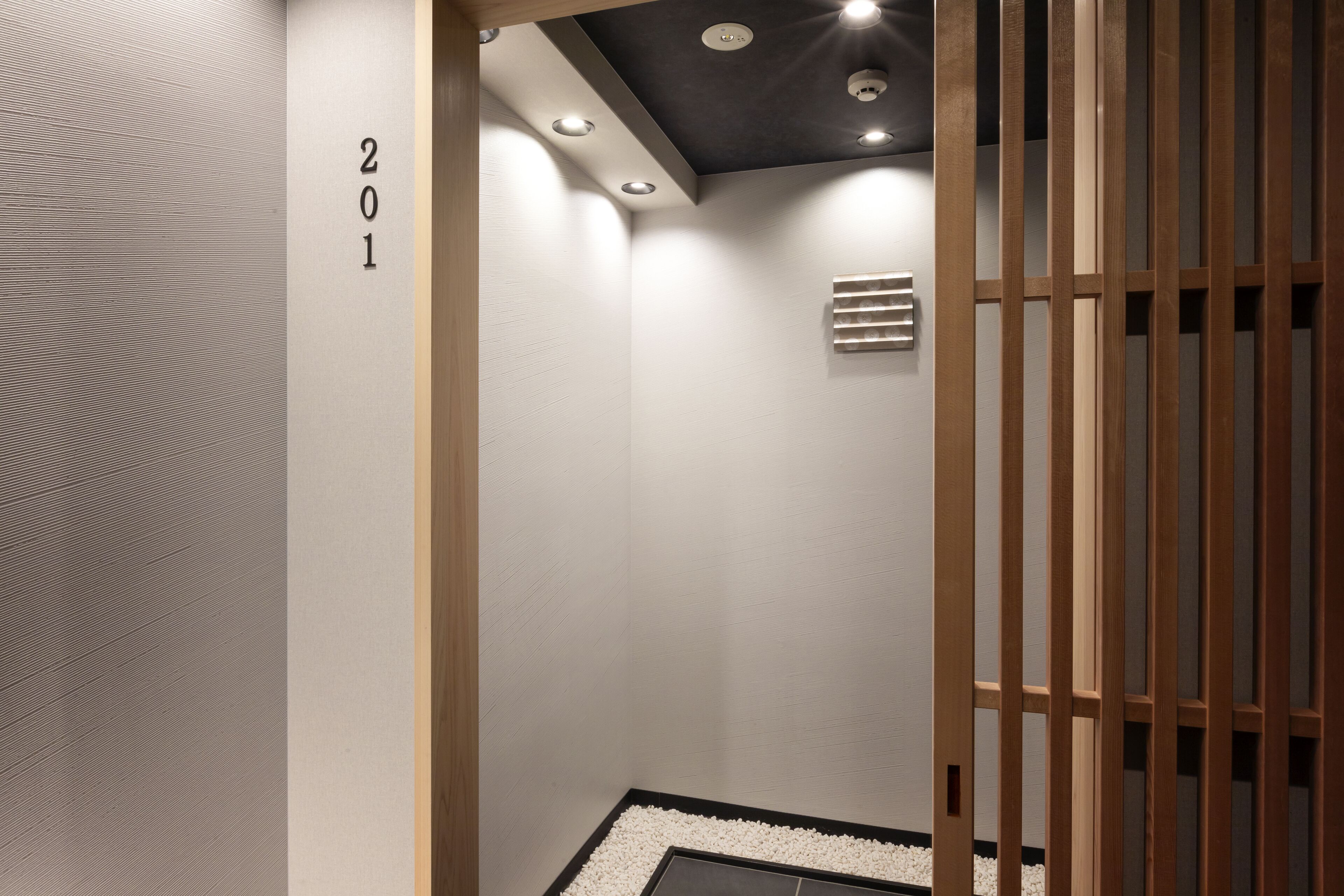 A modern interior with a wooden partition, a number '201' on the wall, and recessed ceiling lights.